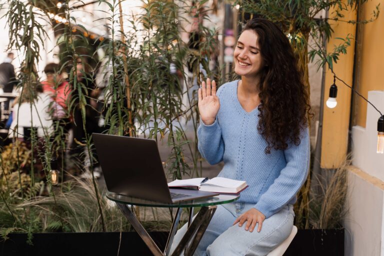 Confident girl with laptop communicates and talks about herself via video communication in cafe outside. Online job interview of girl candidate with HR manager in IT company outdoor