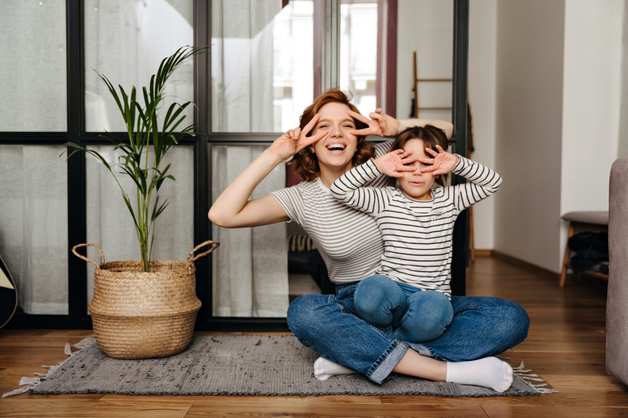 Joyful woman and her daughter having fun in living room and showing signs of peace